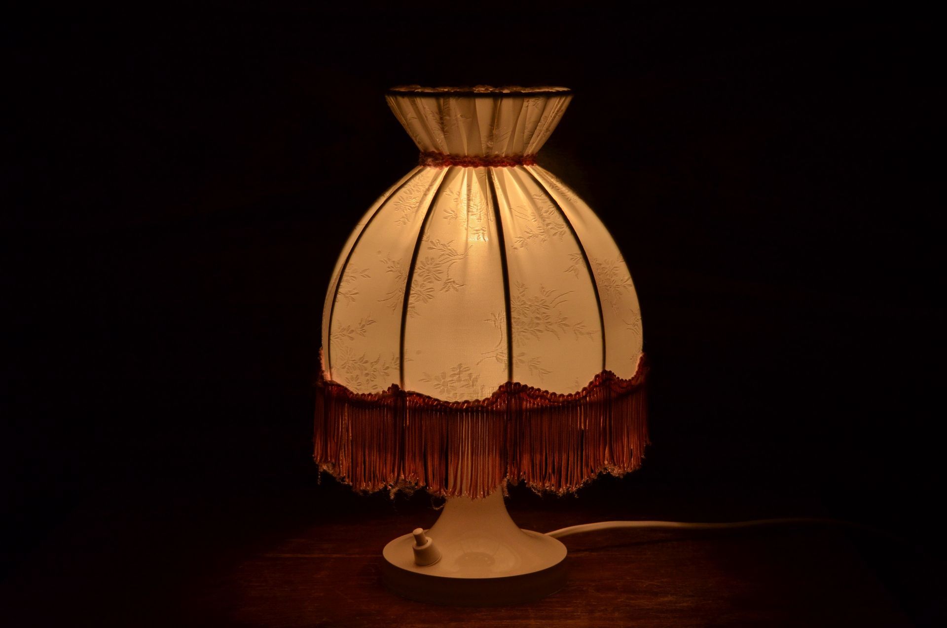 Une lampe de chevet ancienne avec un abat-jour en tissu et des franges
