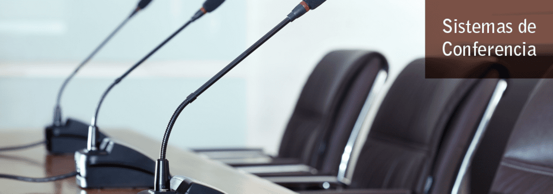 Mesa de conferencias con micrófonos, sillas marrones y texto