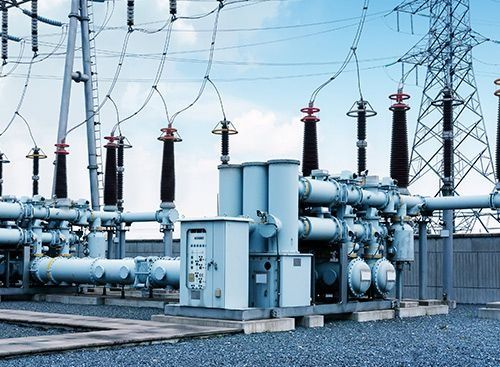 Subestación eléctrica con equipos grises y azules, líneas eléctricas y cielo azul.