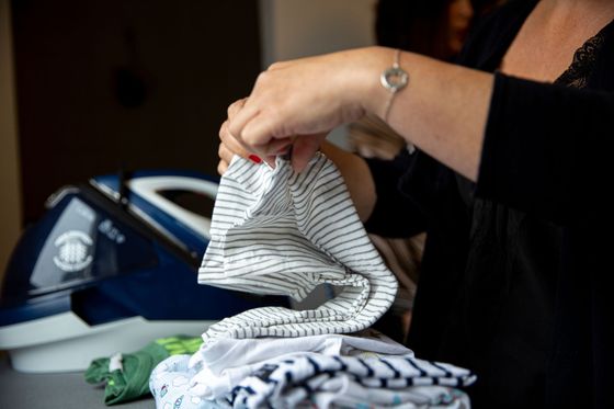Des mains plient du linge rayé à côté d'une planche à repasser et de vêtements empilés.