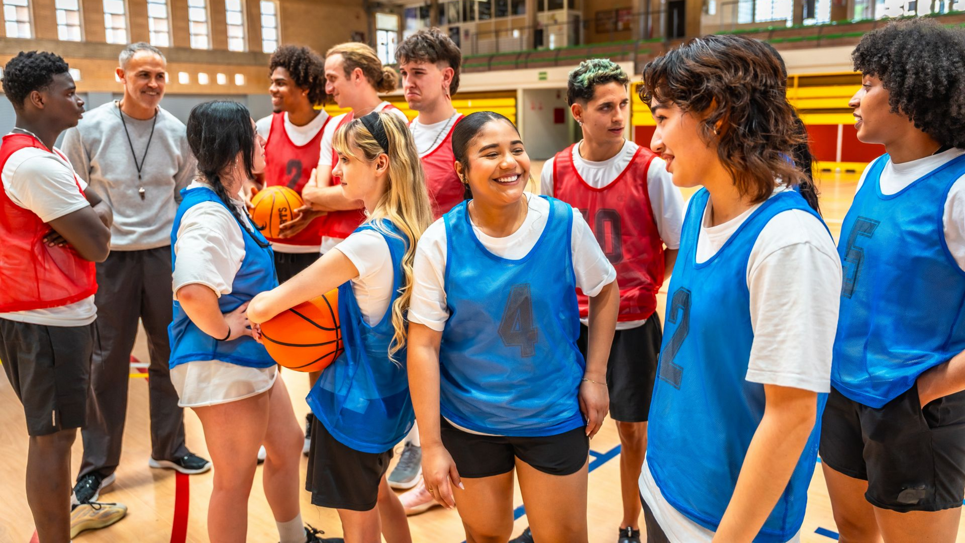 L'équipe de basket-ball se rassemble autour de son entraîneur sur le terrain, vêtue de gilets rouges et bleus.