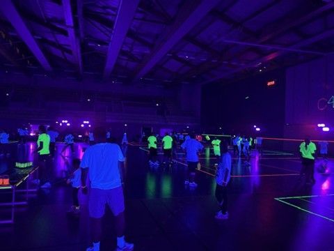 Des personnes pratiquant un sport dans une salle de sport sous des lumières noires, vêtues de vêtements fluo.