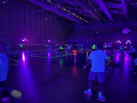 Des personnes pratiquant un sport dans une salle de sport éclairée par des lumières UV violettes, des lignes fluorescentes et des vêtements qui brillent.
