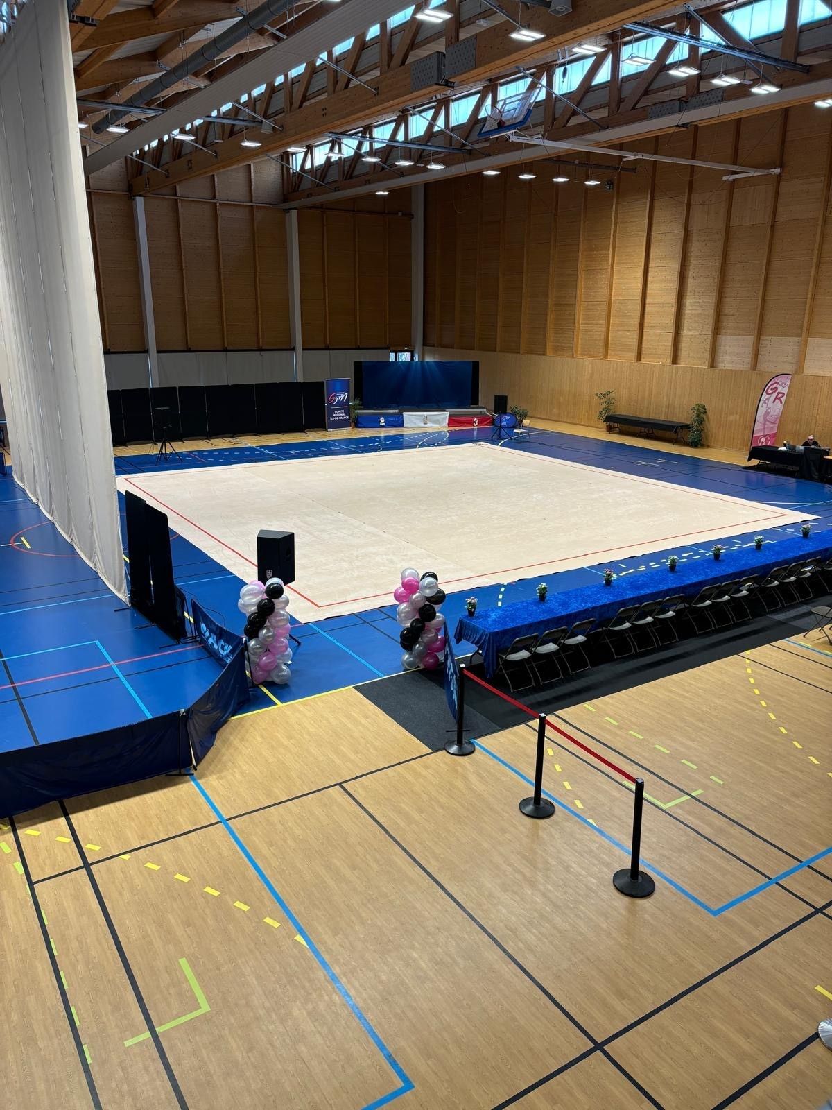 Intérieur d'un gymnase avec un tapis de gymnastique bleu et blanc, des gradins et des boiseries.