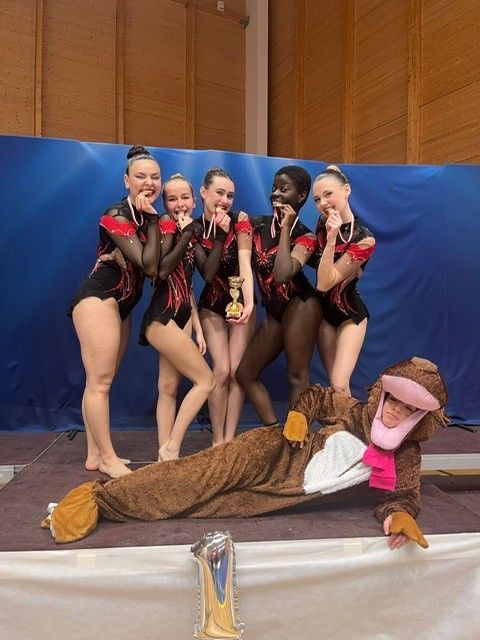 Un groupe de gymnastes posant avec un trophée, une personne déguisée en singe au sol.