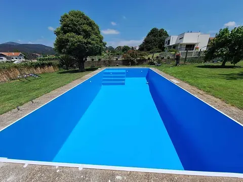 Una gran piscina azul con escaleras rodeada de césped y árboles.