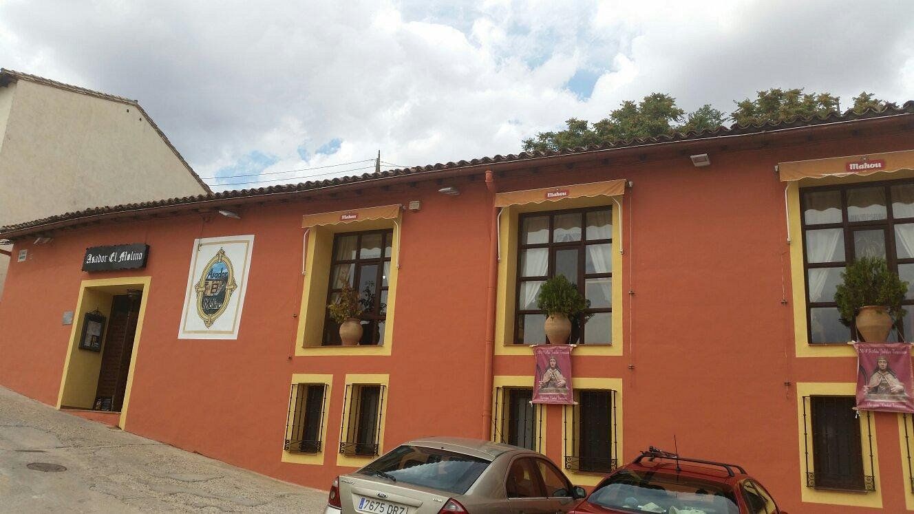 Edificio de estuco naranja con ventanas con marcos amarillos, carteles publicitarios y coches aparcados bajo un cielo nublado.