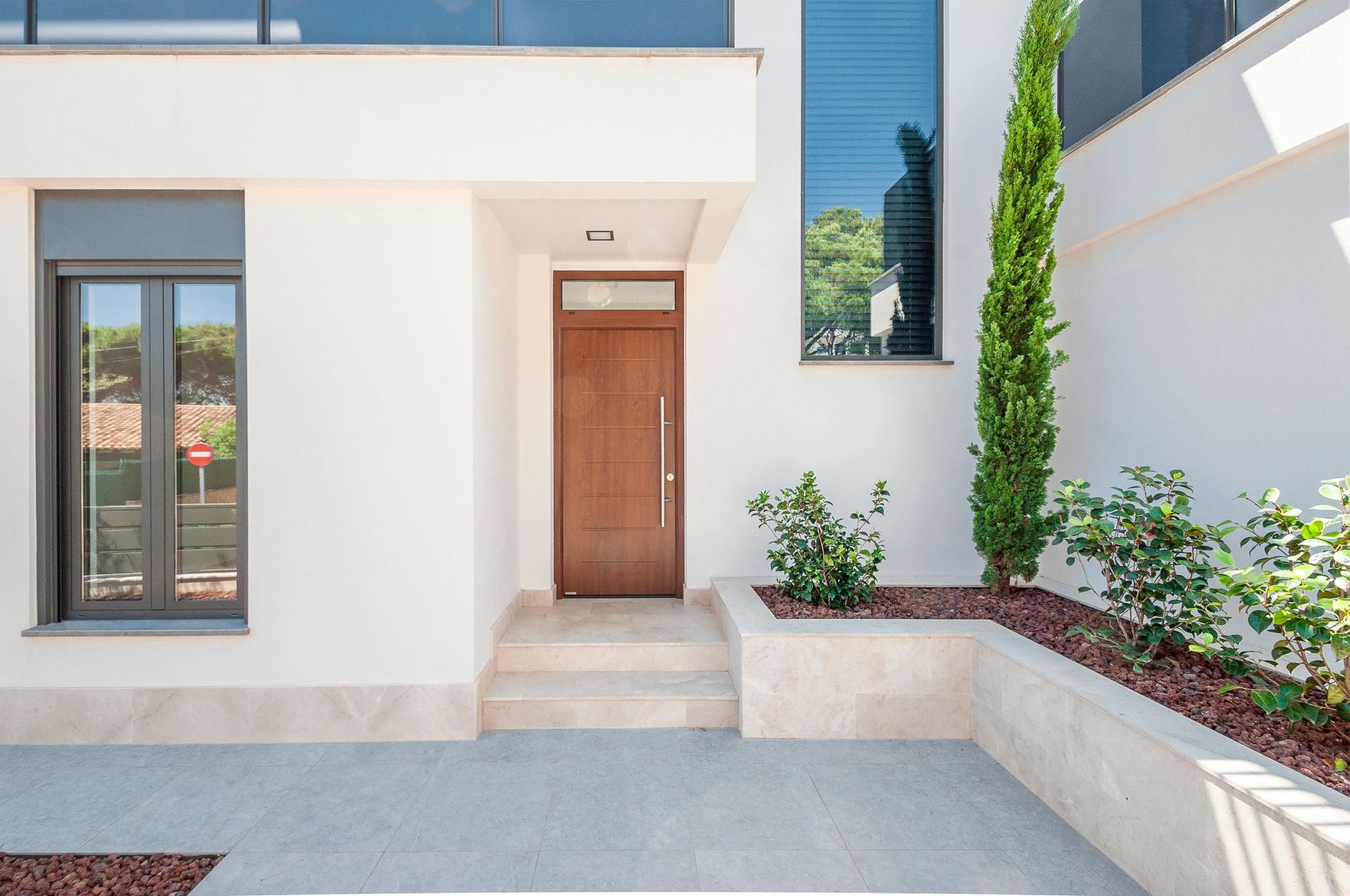 Entrée d'une maison blanche moderne avec porte en bois, marches et cour paysagée