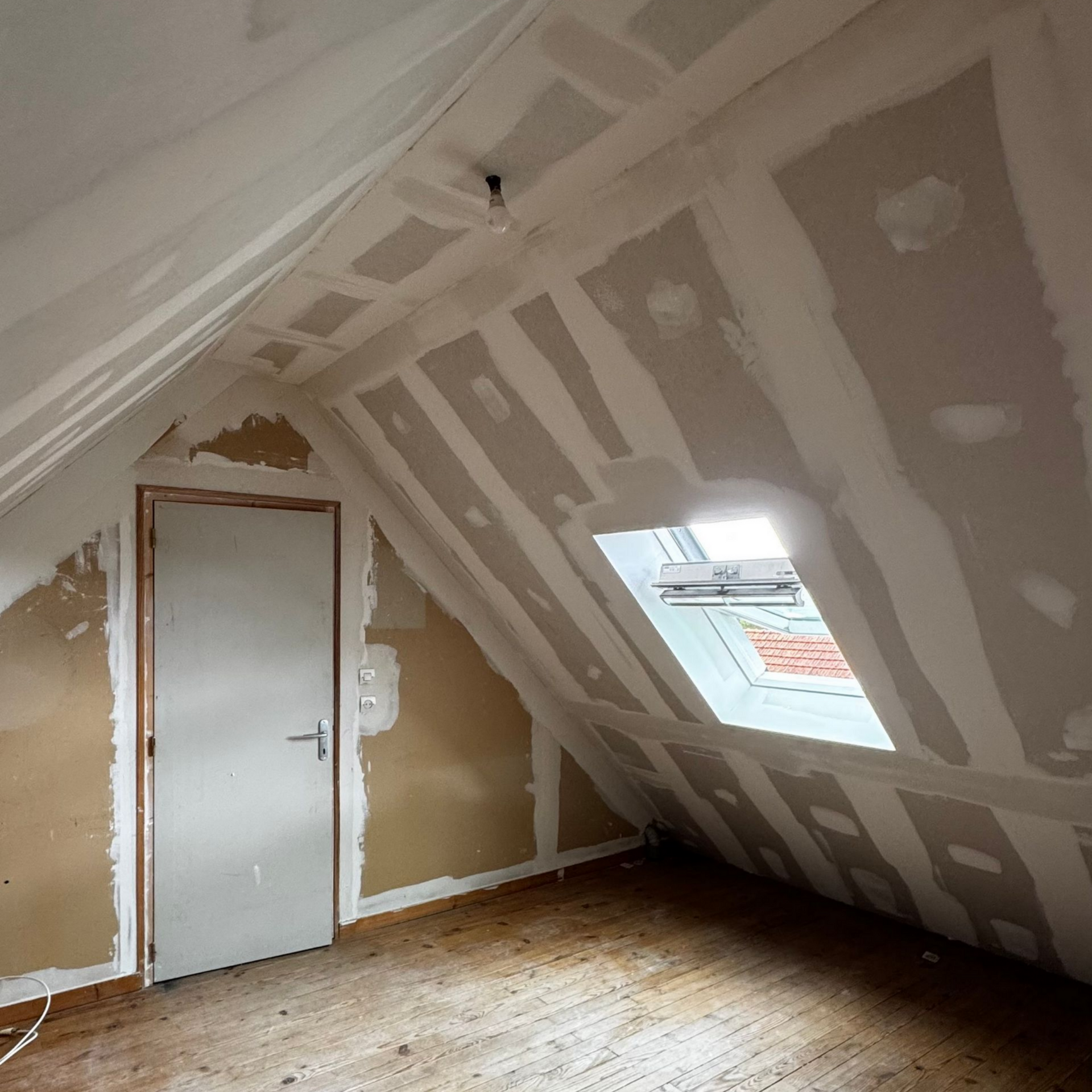 Chambre mansardée lumineuse et minimaliste avec un lit, un puits de lumière et une commode blanche sur un parquet clair