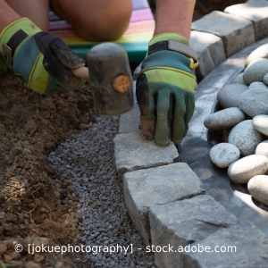 Eine Person verlegt mit einem Hammer Steine in einem Garten. Karl Müller Garten- und Landschaftsbau