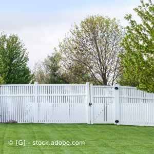 Ein weißer Zaun mit einem Tor inmitten eines üppig grünen Hofes. Karl Müller Garten- und Landschaftsbau