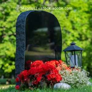 Ein Grabstein mit roten Blumen und einer Laterne auf einem Friedhof. Karl Müller Garten- und Landschaftsbau