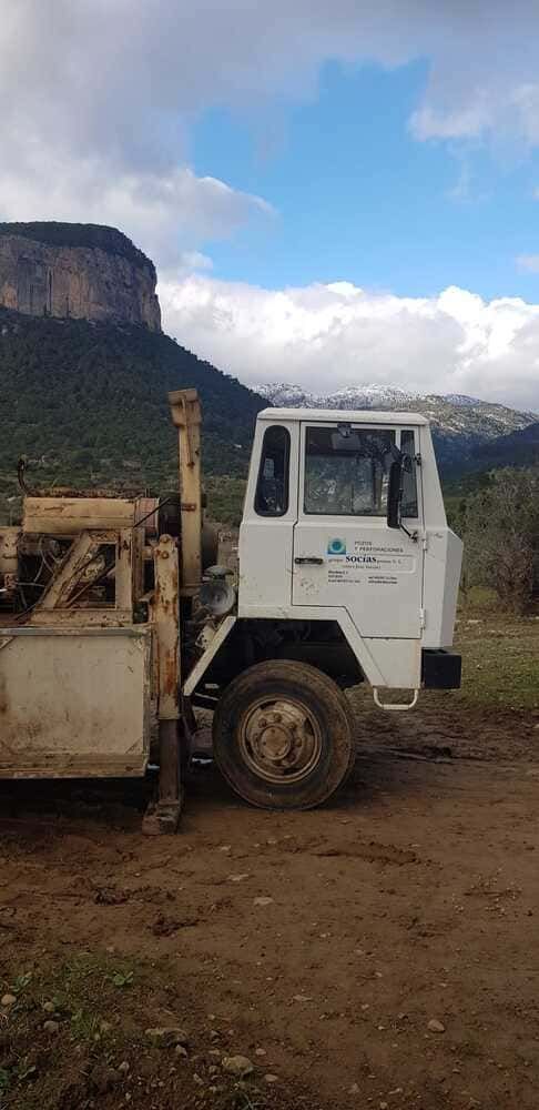 Un camión blanco está estacionado al costado de un camino de tierra frente a una montaña.