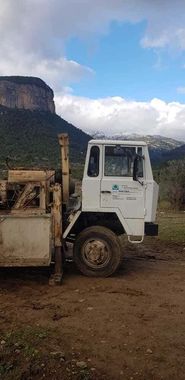 Un camión blanco está estacionado al costado de un camino de tierra frente a una montaña.