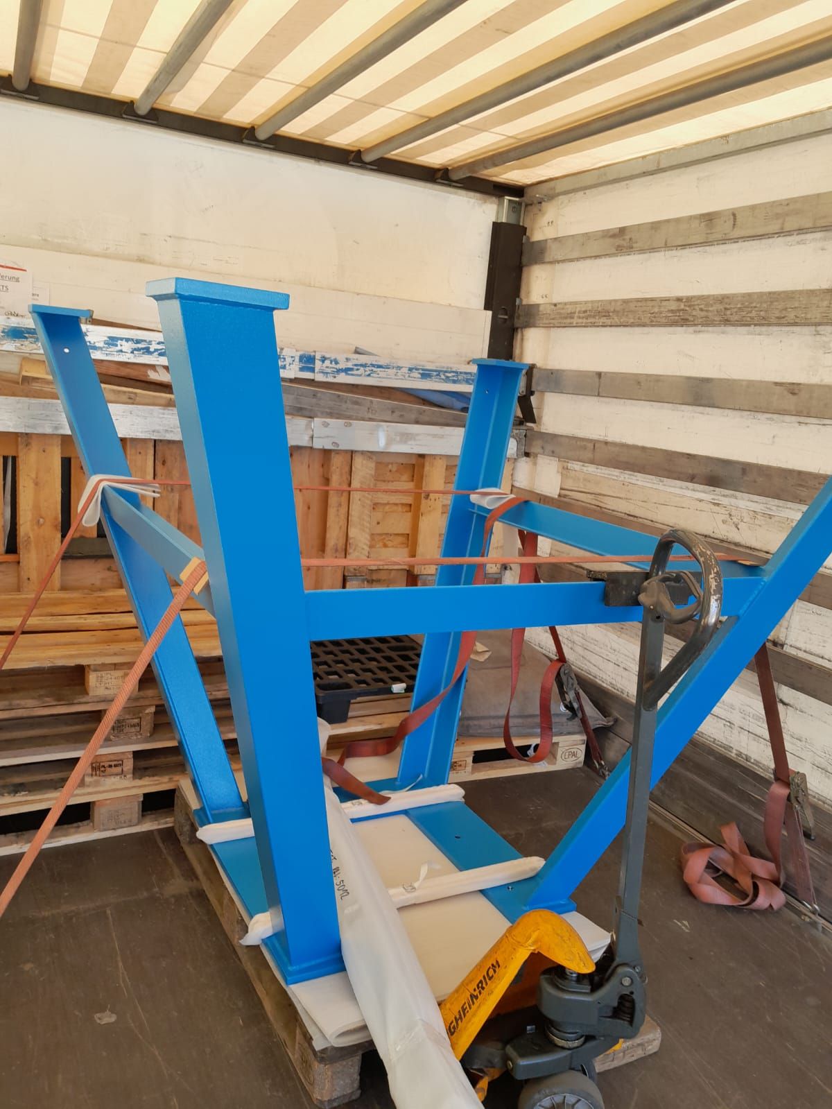 Ein blaues Metallgestell ist auf Paletten im Inneren eines LKW befestigt. Ein Hubwagen steht davor.