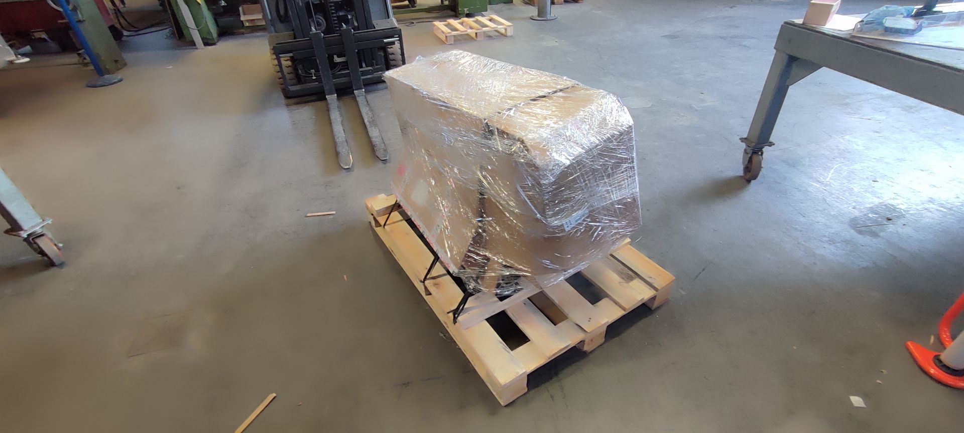 Ein in Plastikfolie eingewickelter Motor auf einer Holzpalette in einer Lagerhalle.