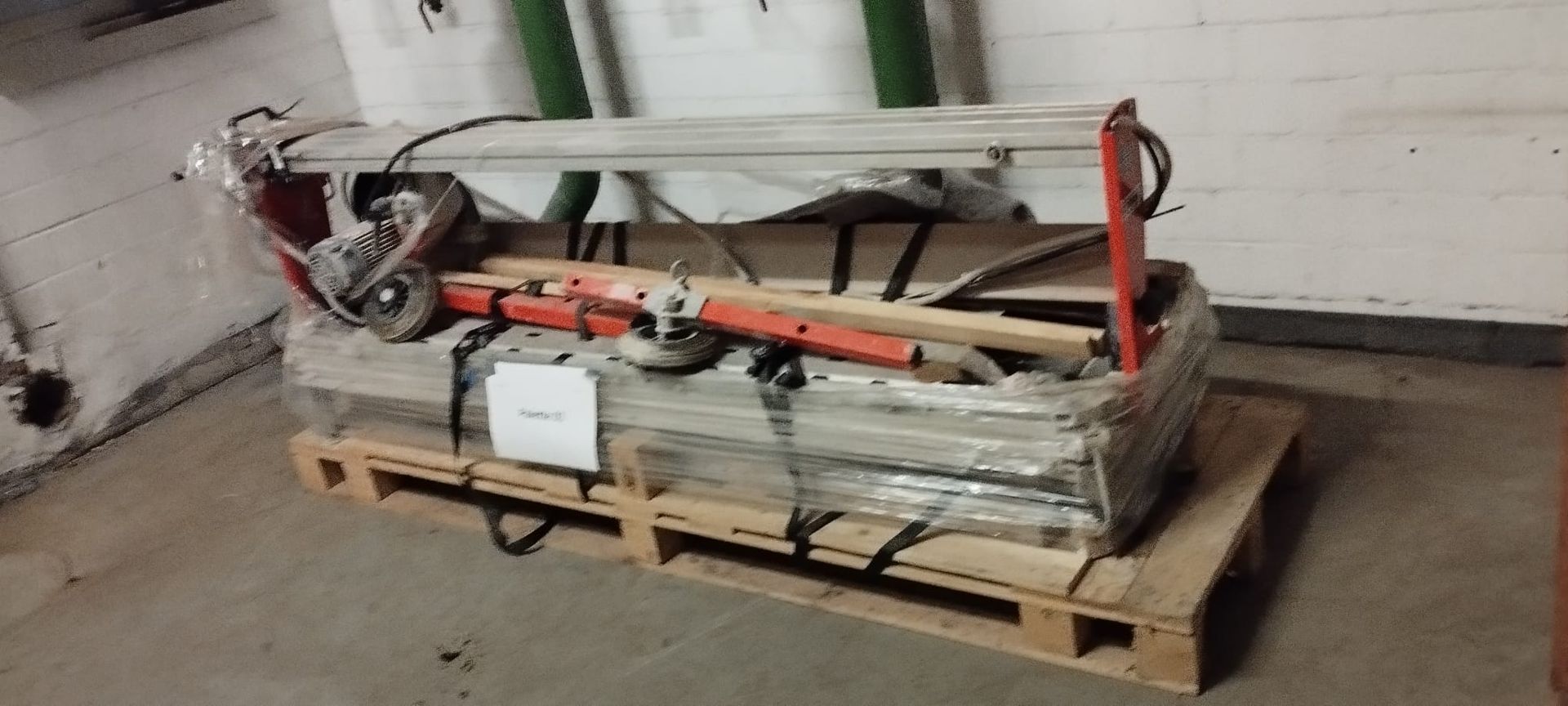 Eine mit Plastikfolie umwickelte Palette, die Bauwerkzeuge, darunter eine rote Säge, enthält.