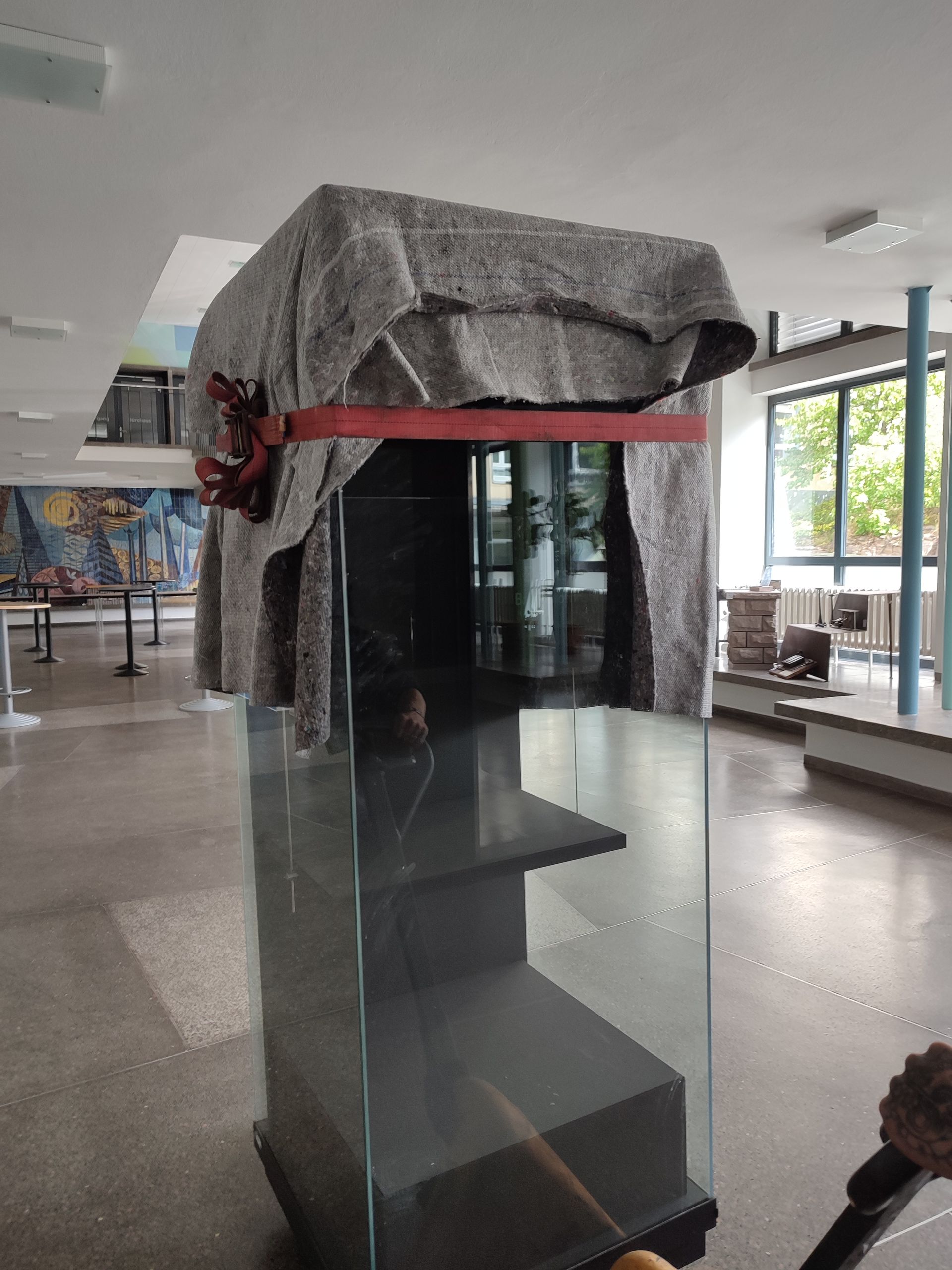 Eine mit grauem Stoff verkleidete Glasvitrine in einem Museum. Ein rotes Band ziert den Stoff.