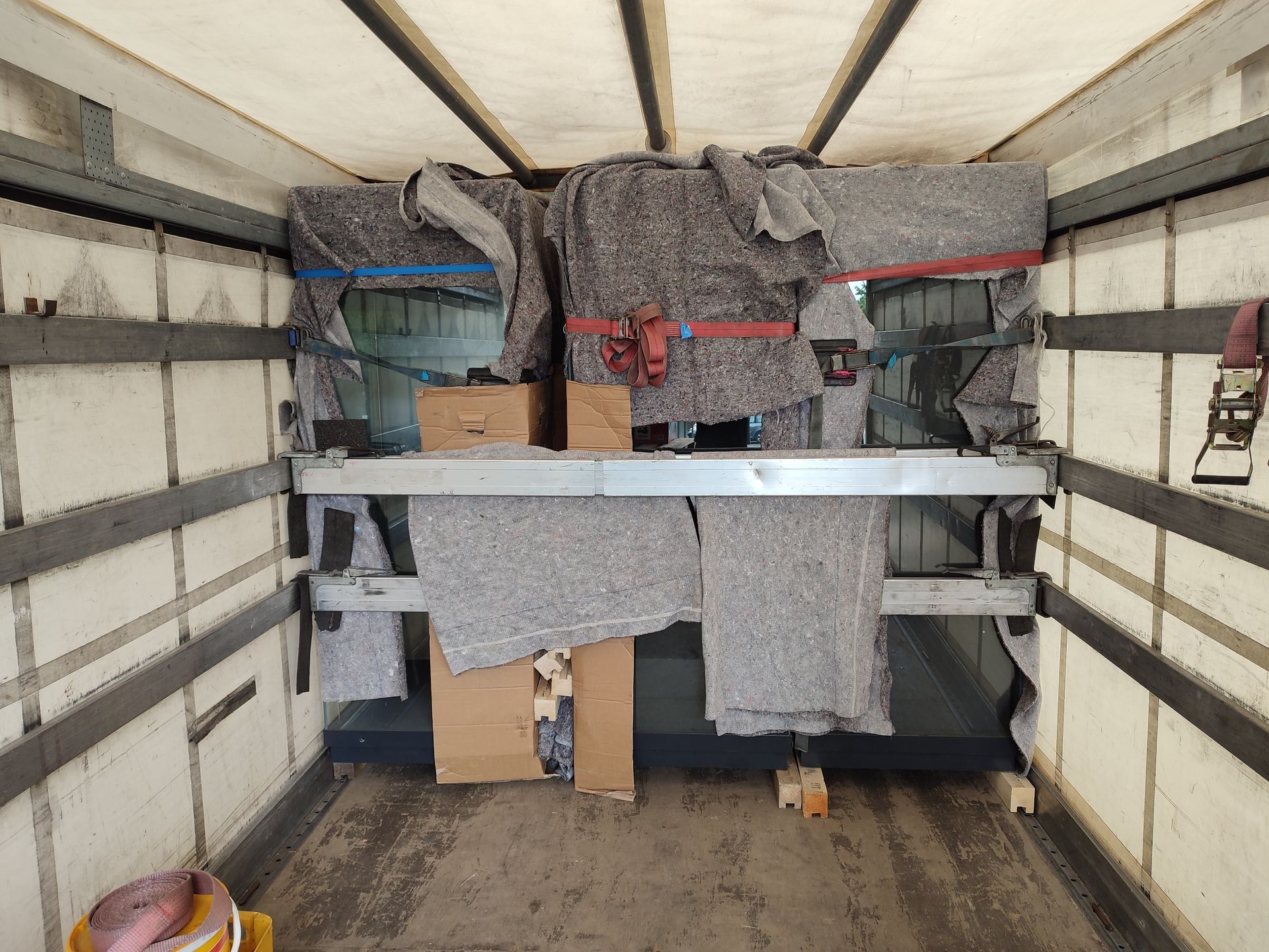 Innenraum eines LKW-Laderaums mit Regalen, Kartonagen und Schutzdecken.