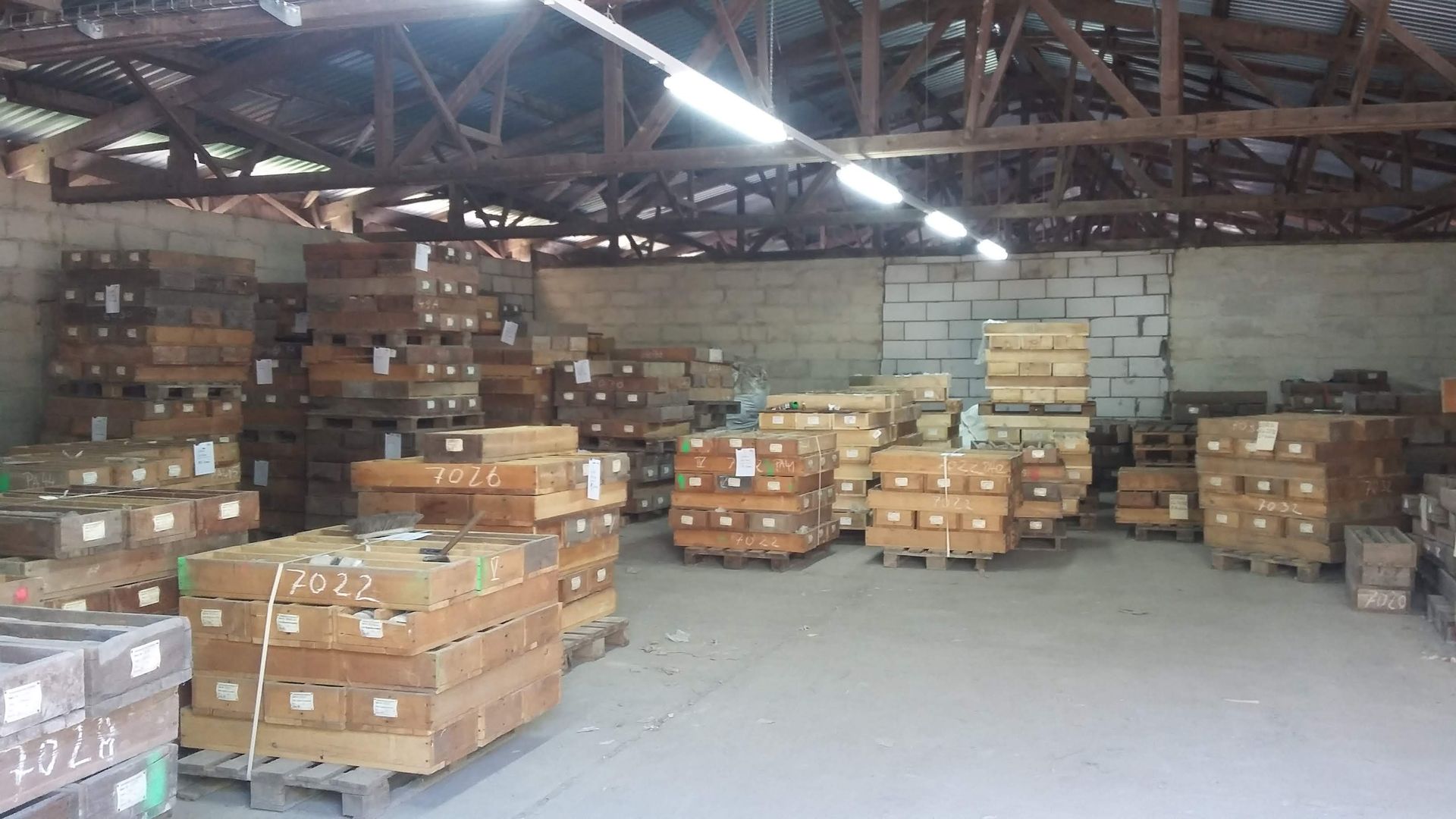 Innenansicht einer Lagerhalle mit gestapelten Holzkisten auf Paletten unter einer Holzbalkendecke.