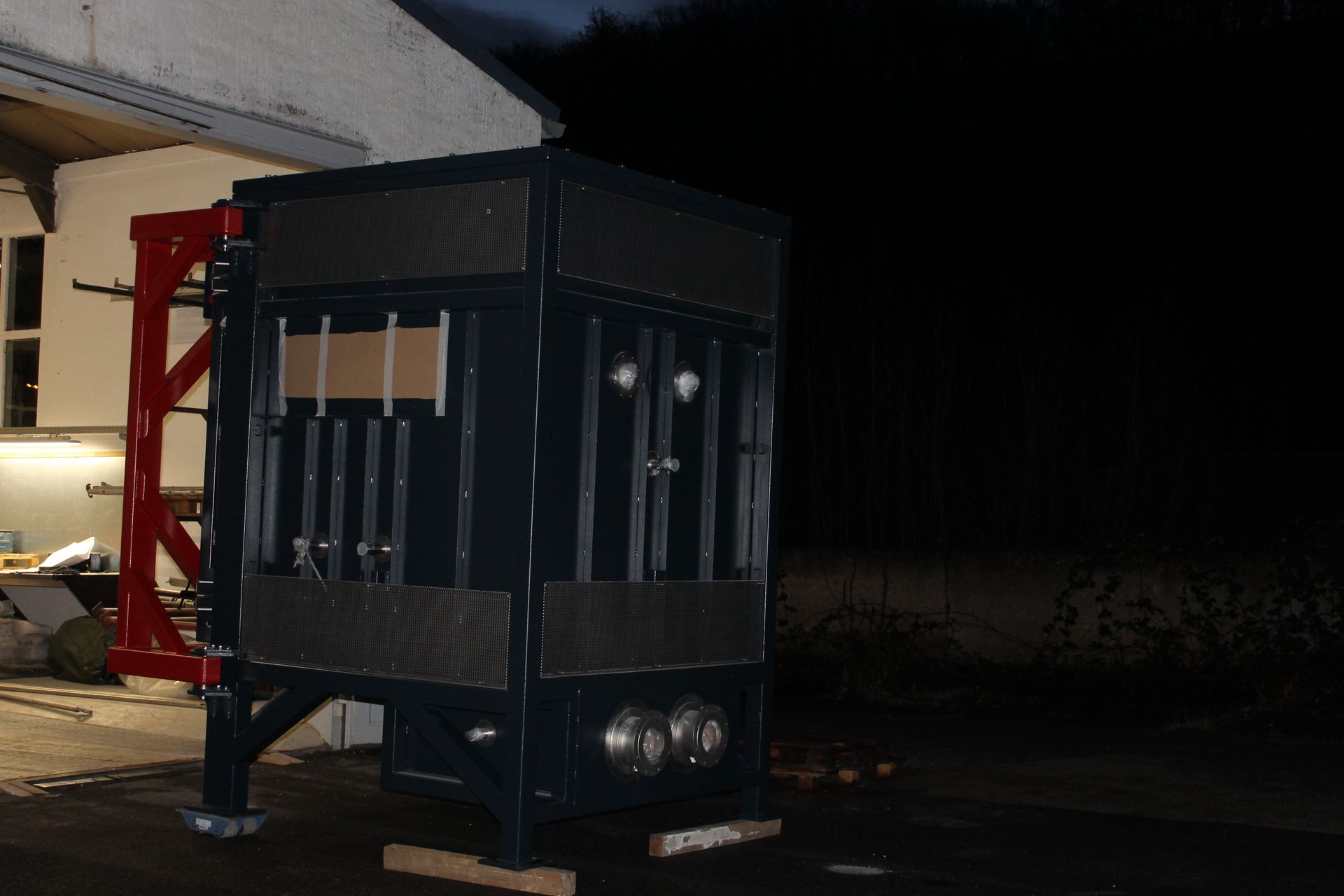 Dunkelblaue, rechteckige Maschine mit Metallrahmen, draußen bei Nacht. Rote Stützkonstruktion auf der linken Seite.