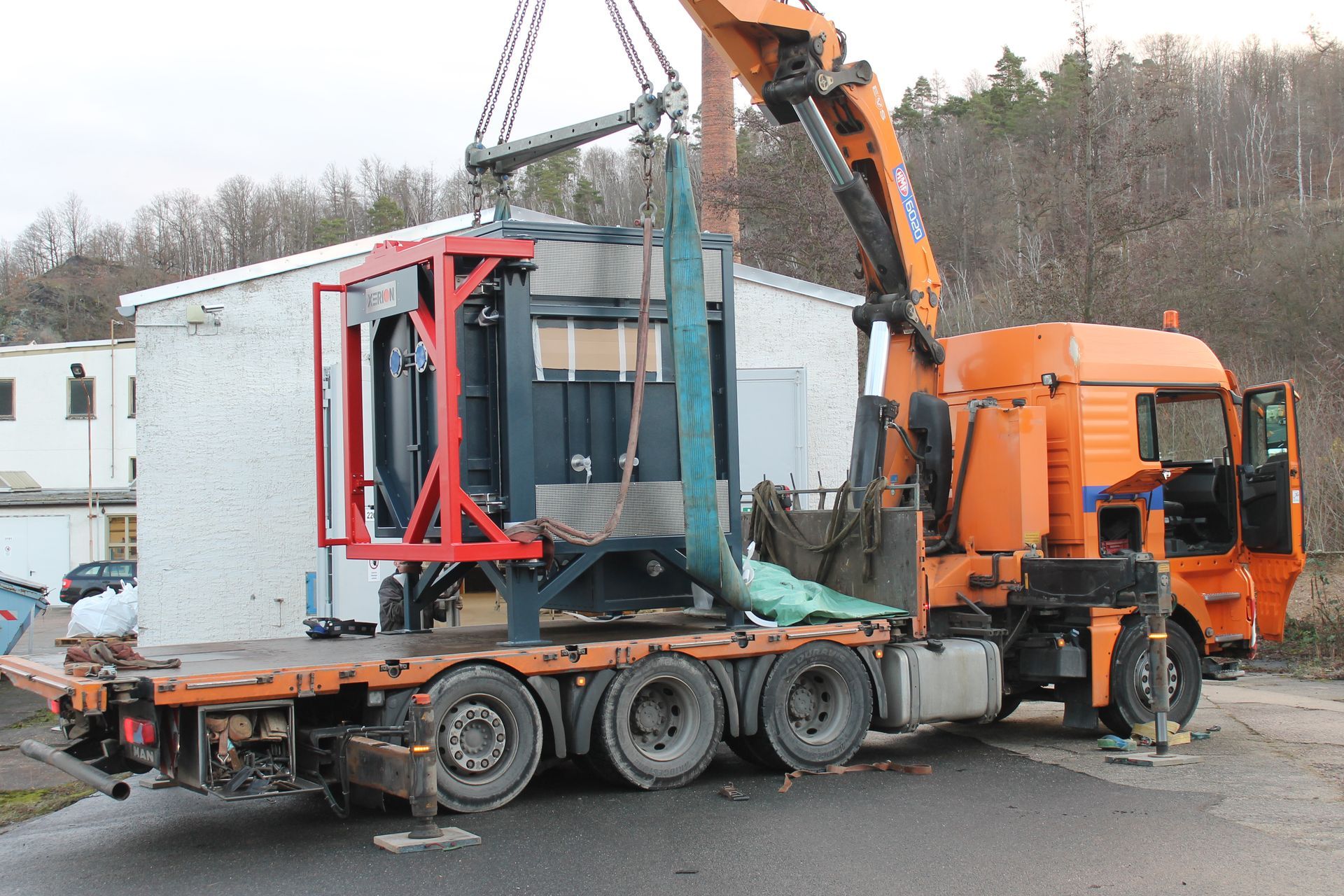 Ein Kran hebt eine große Industriemaschine von einem Tieflader.