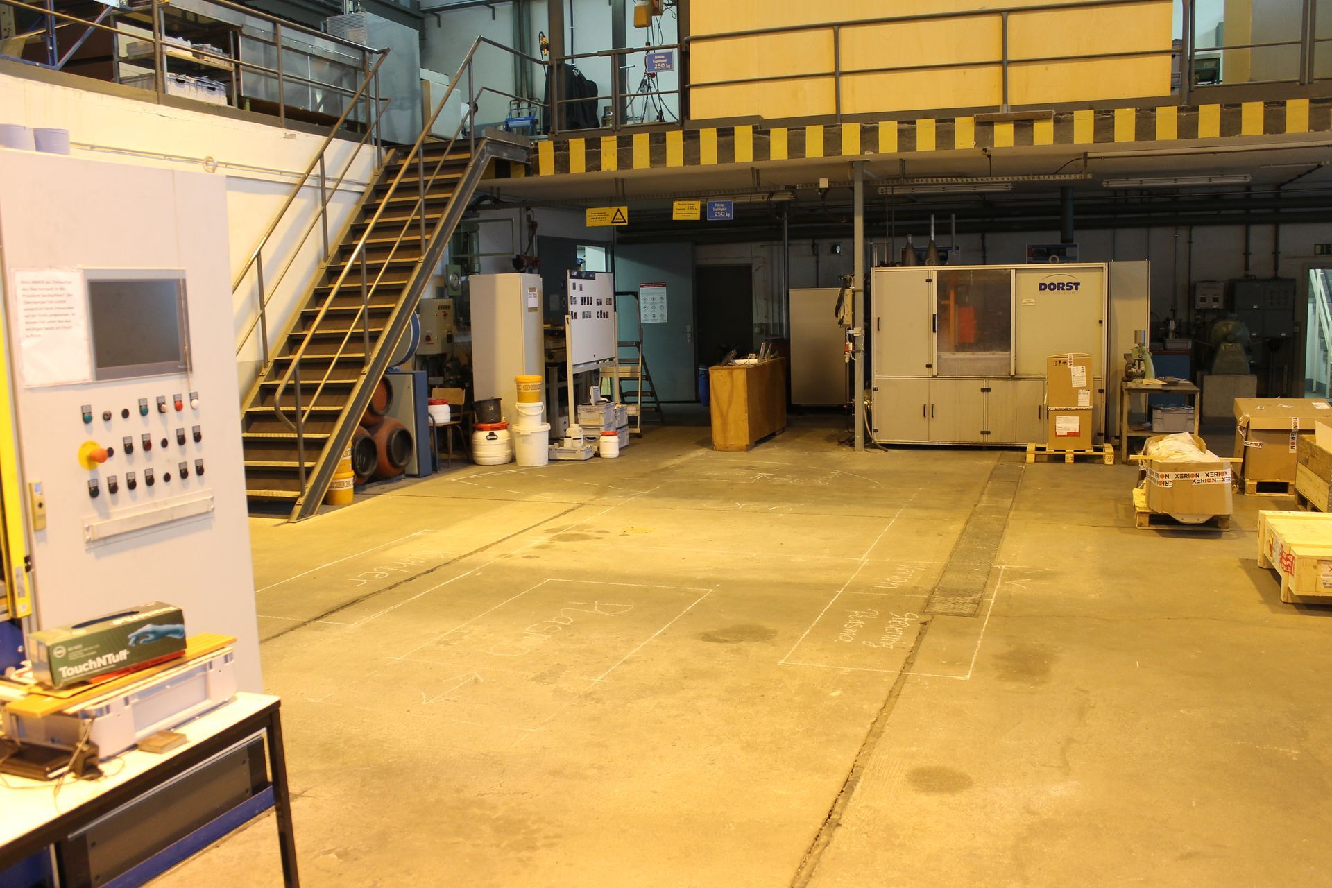 Innenansicht einer Industriehalle mit Maschinen, Treppe und Bedienfeld.