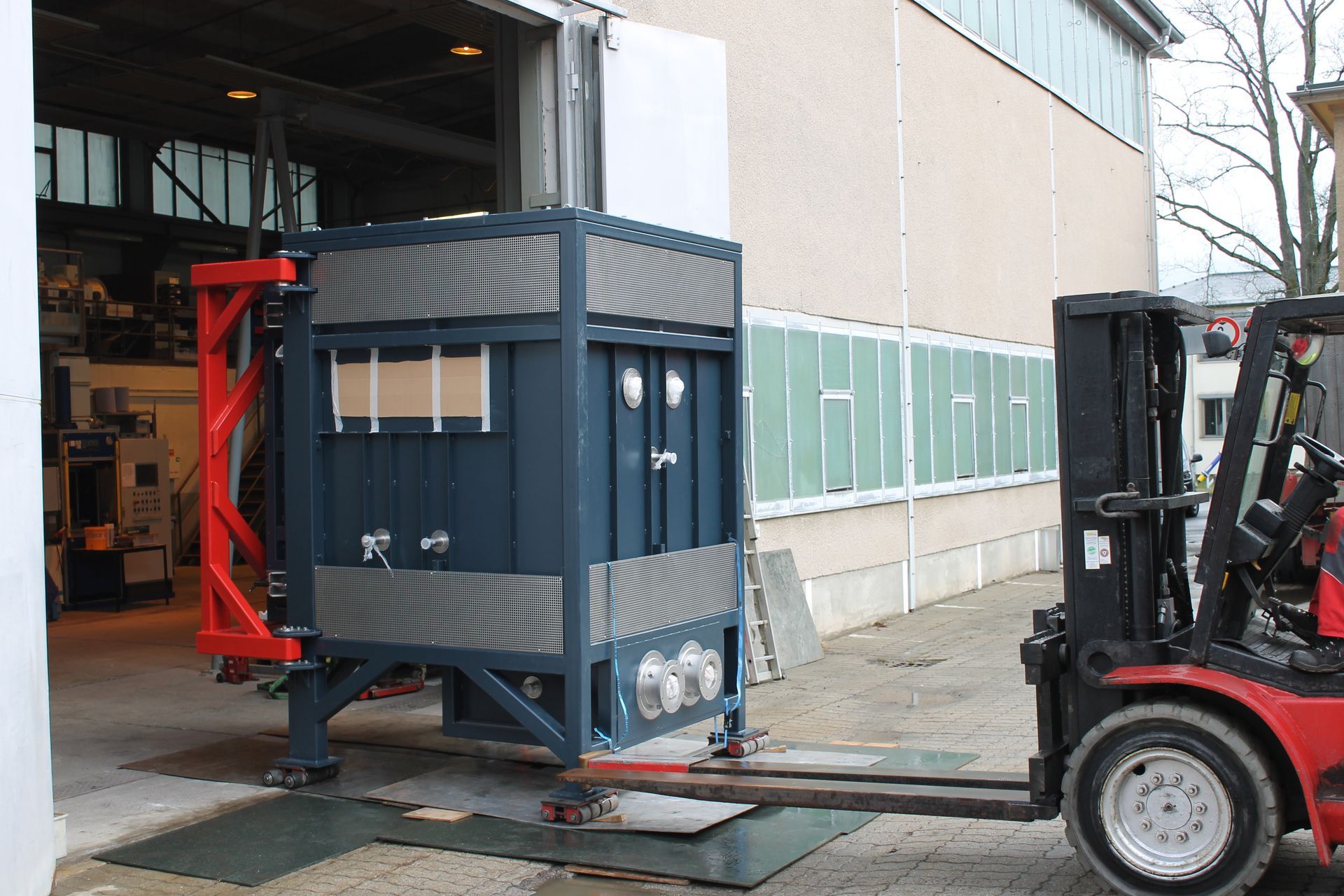 Ein Gabelstapler transportiert eine blaue Industrieeinheit aus einem Lagertor. Roter Gabelstapler und Rahmen.