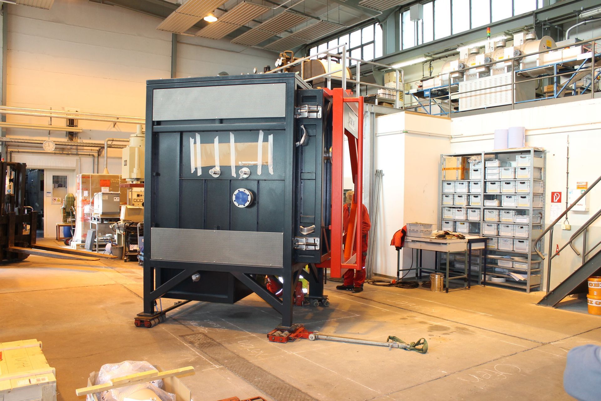 Schwarze und rote Metallkonstruktion in einer Laborumgebung mit Werkzeugen, Maschinen und Lagerraum.