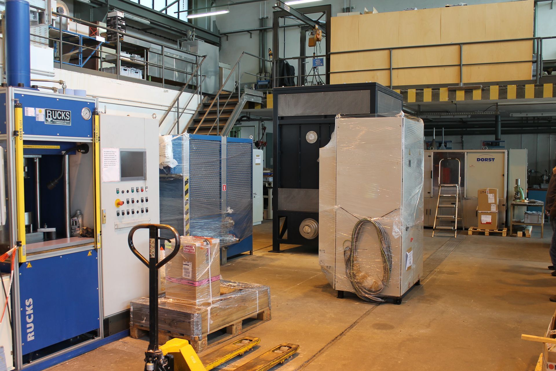 Fabrikinterieur mit Maschinen und Anlagen; einige Gegenstände sind verpackt. Im Vordergrund ist ein Gabelstapler zu sehen.