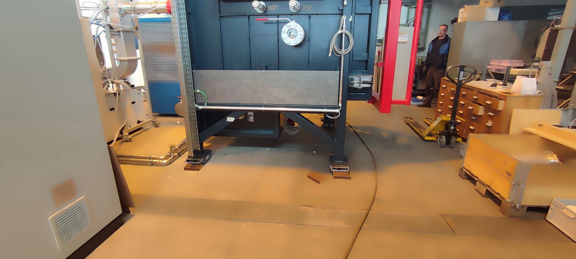 Eine große Industriemaschine in einer Werkstatt. Im Hintergrund steht eine Person.