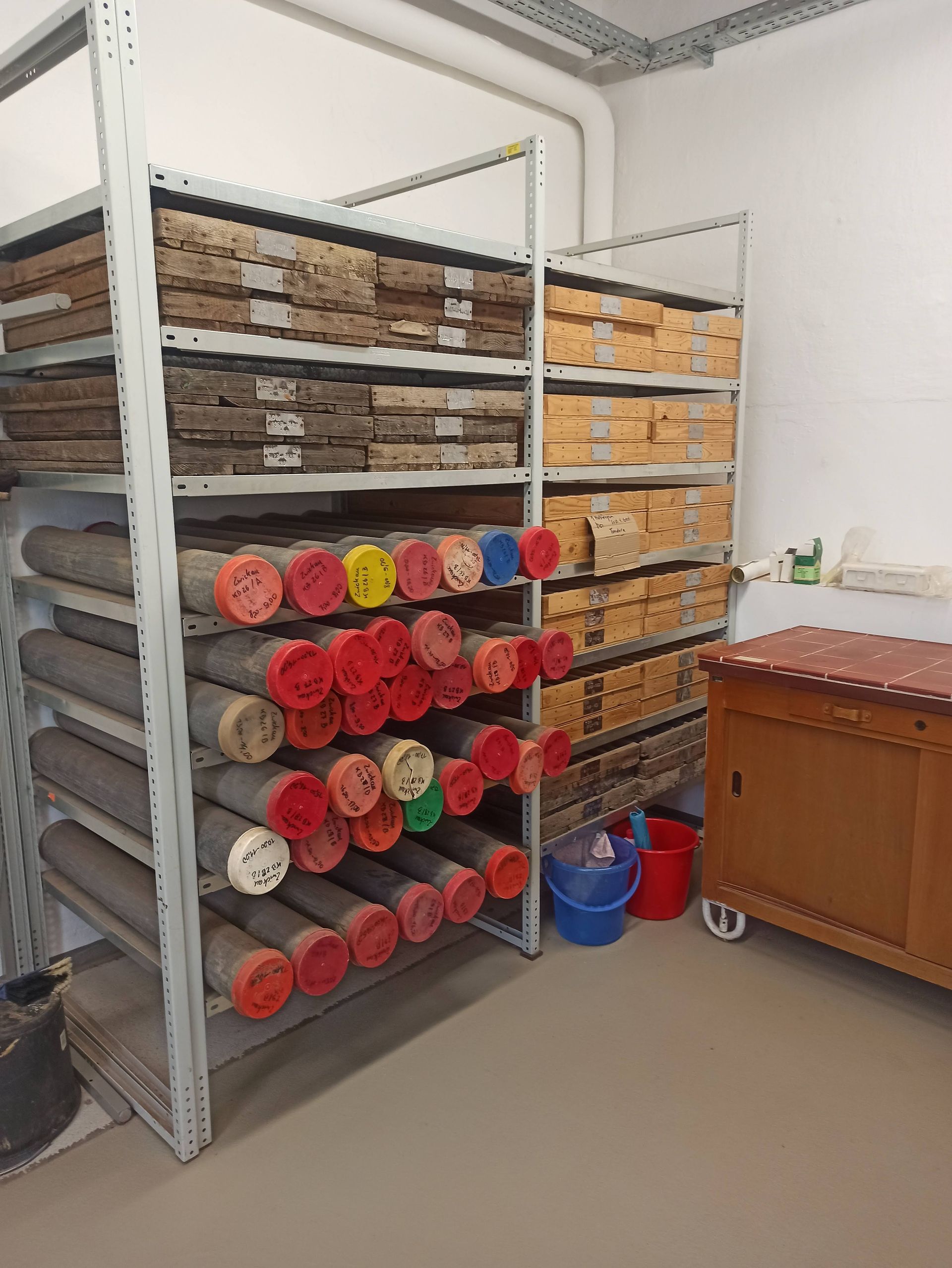 Regale mit gerollten Röhren mit roten Deckeln und Schachteln; in einem Lagerraum.
