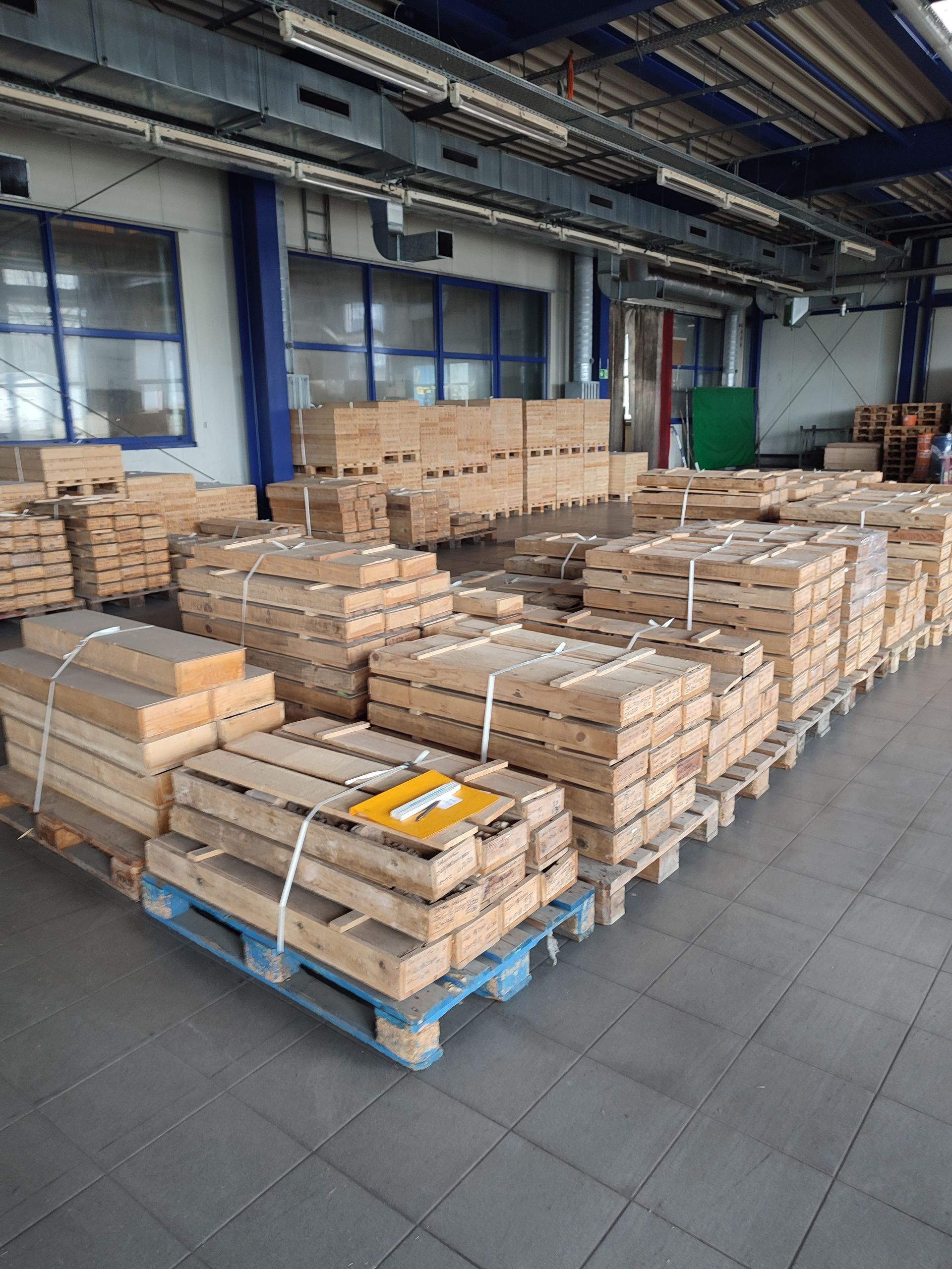 In einer Lagerhalle sind Holzkisten auf Paletten gestapelt.