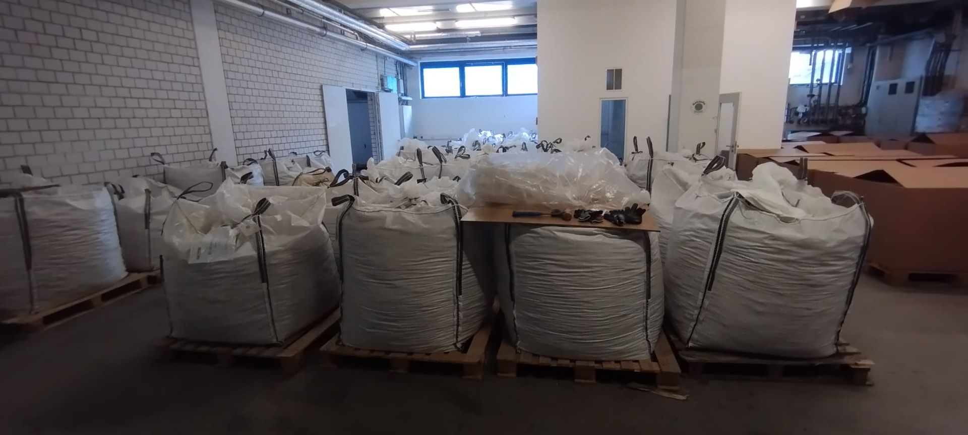 Große weiße Säcke auf Paletten in einem Lagerhaus. Helle Beleuchtung, industrielles Ambiente.