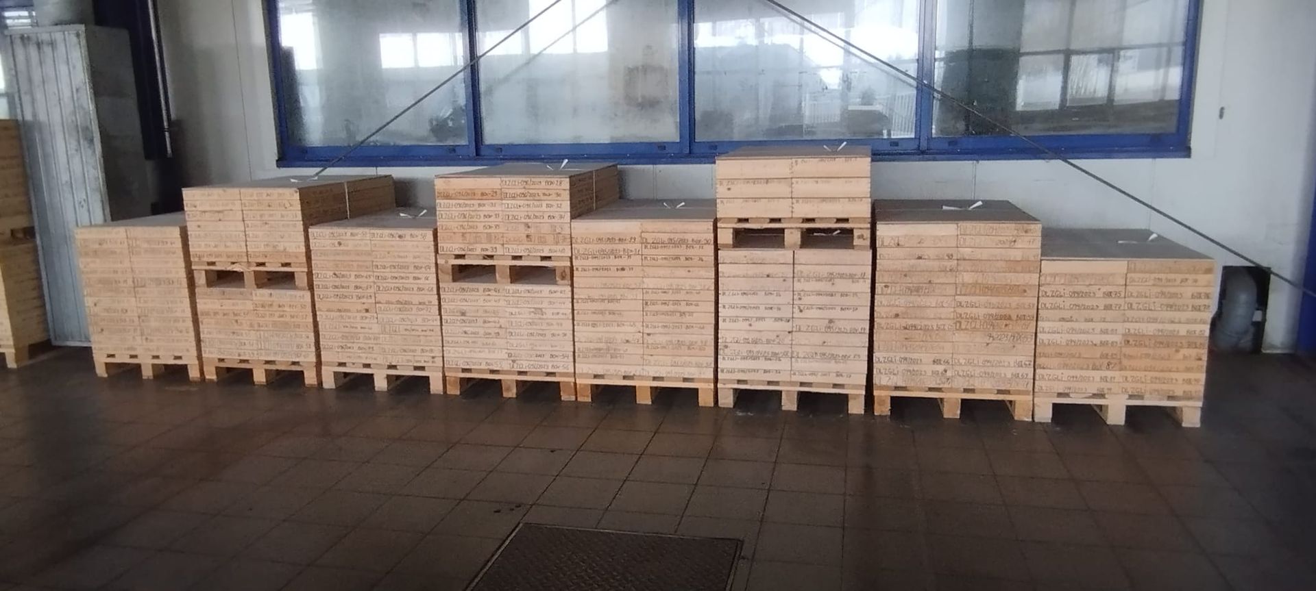 In einer Industrieumgebung, neben einem Fenster, sind Holzkisten auf Paletten gestapelt.