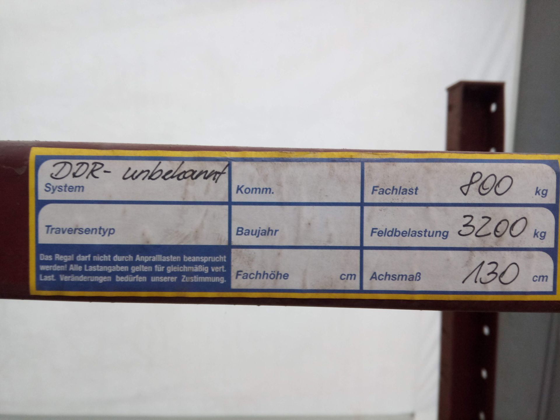 Auf einem Metallträger befindet sich ein Etikett mit deutscher Beschriftung, das die Tragfähigkeit und weitere technische Daten angibt.