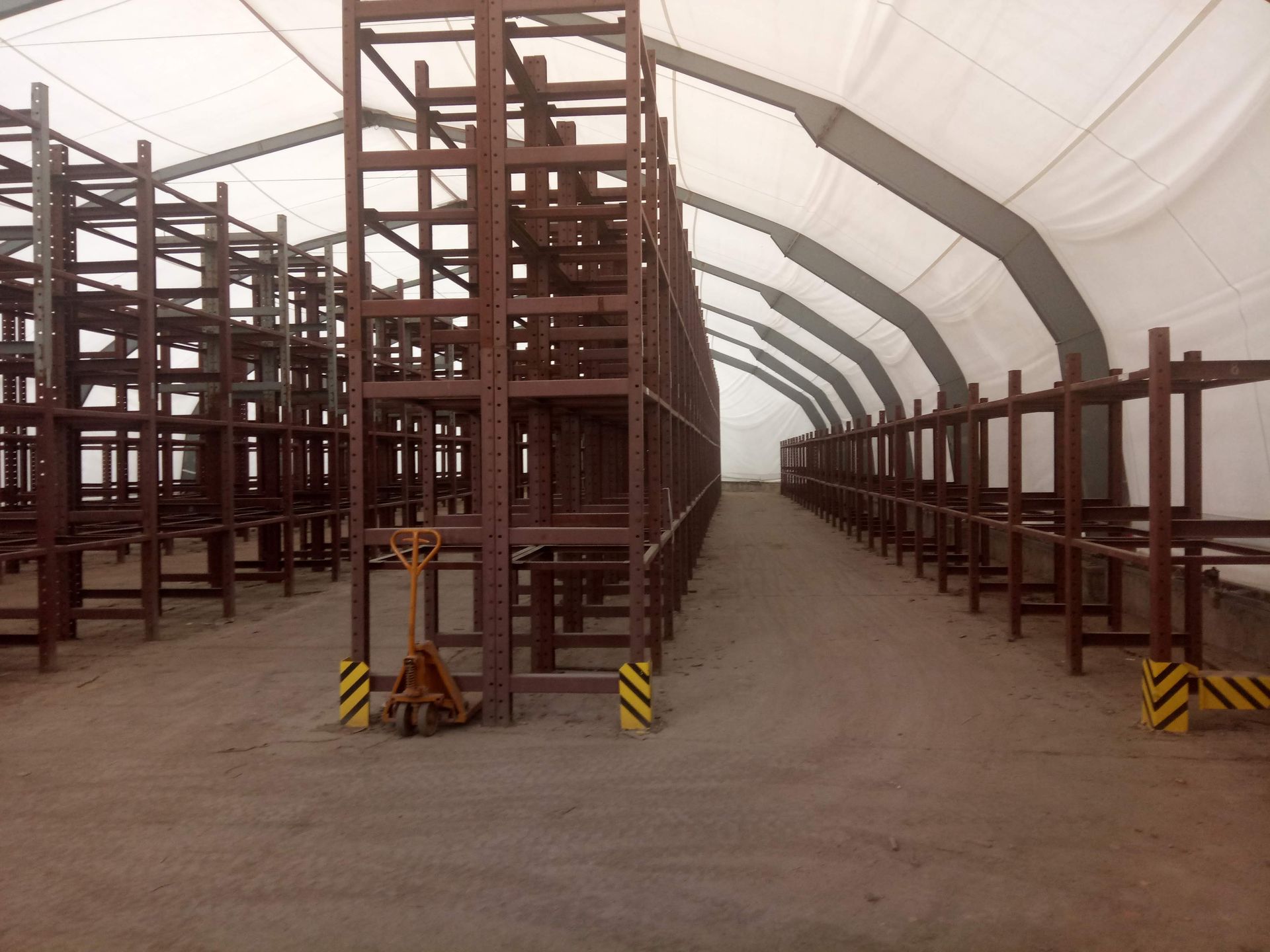 Lagerhalleninnenraum mit Metallregalen unter einem weißen, zeltartigen Dach. Leerer, unbefestigter Boden.