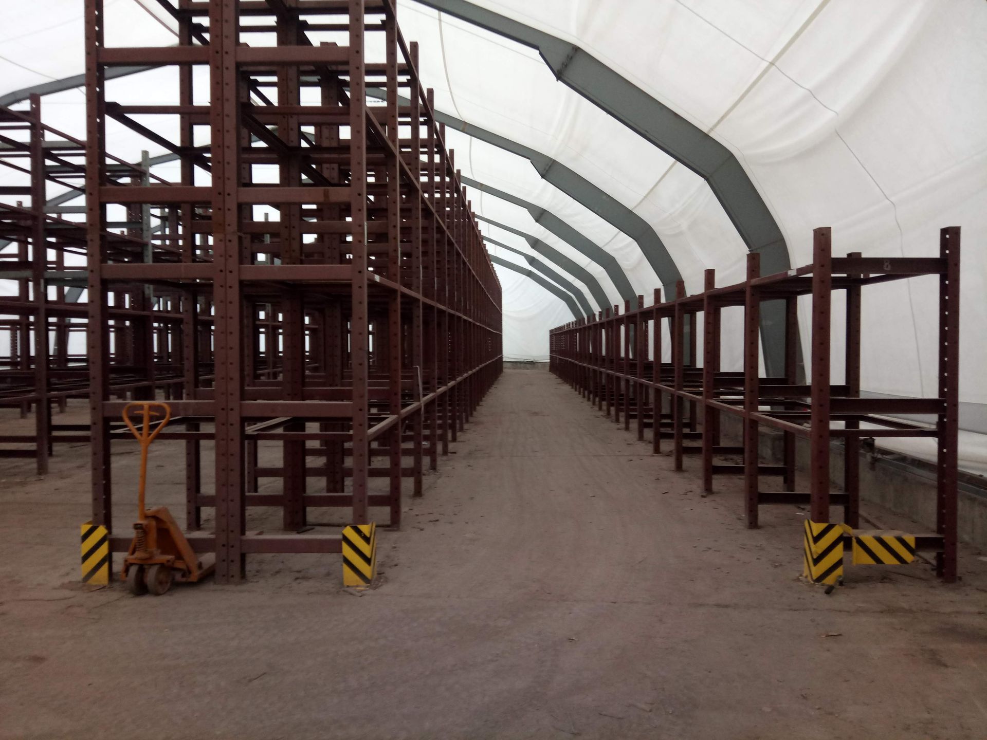 Reihen leerer Metallregale in einer großen Lagerhalle mit weißem Dach. Ein Sackkarren steht neben den Regalen.