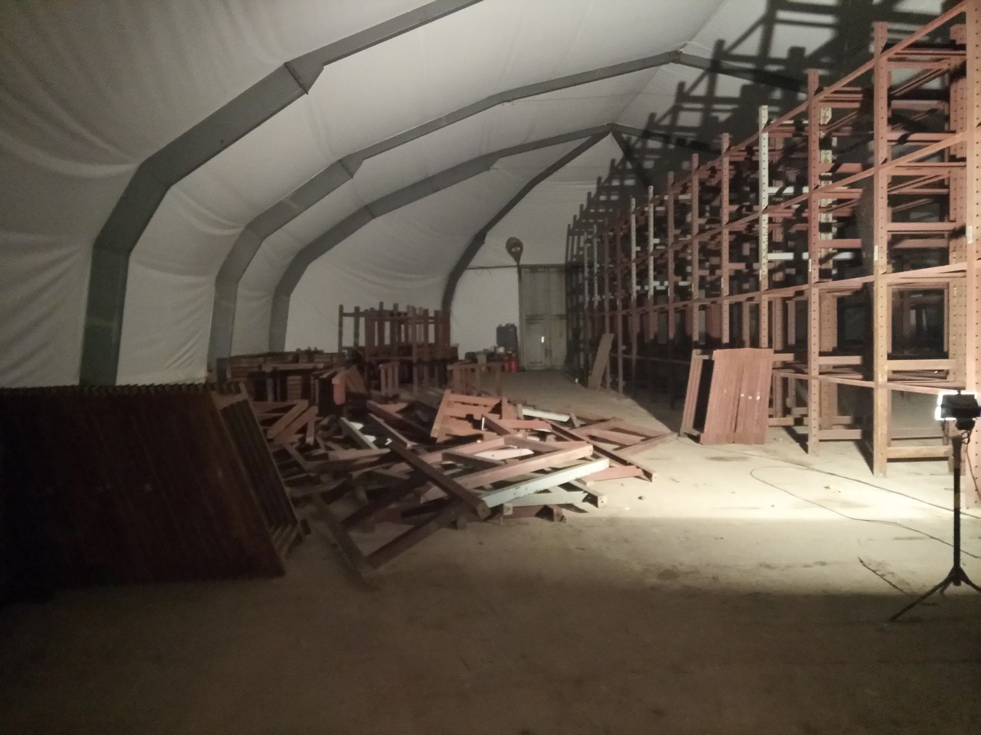 Innenansicht eines großen Lagerzeltes mit Holzregalen, Schutt und einem Scheinwerfer.