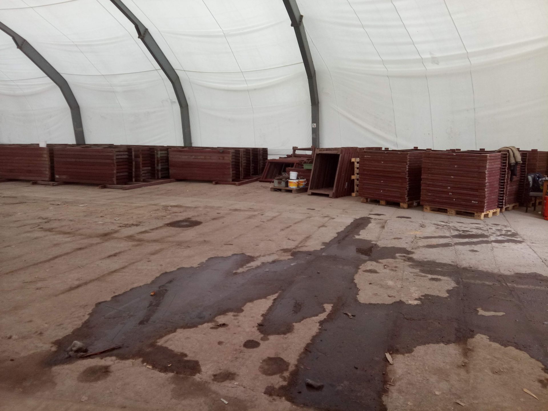 Lagerhalleninneres mit Paletten aus rötlich-braunem Holz. Nasser Boden, weißes Dach.