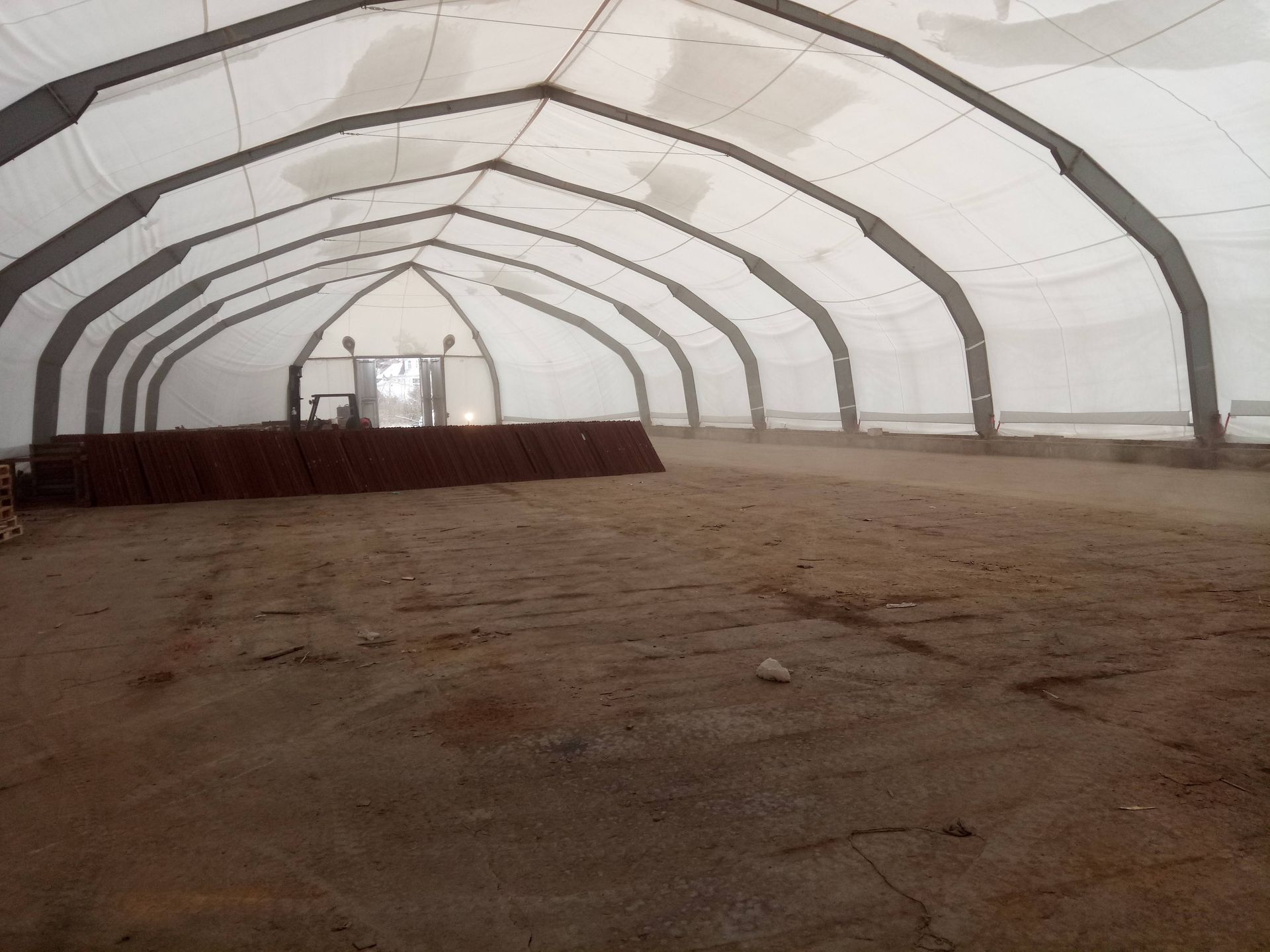 Großes, leeres Zeltinneres; Lehmboden, gewölbte Metallträger, weißes Stoffdach und weiße Wände.