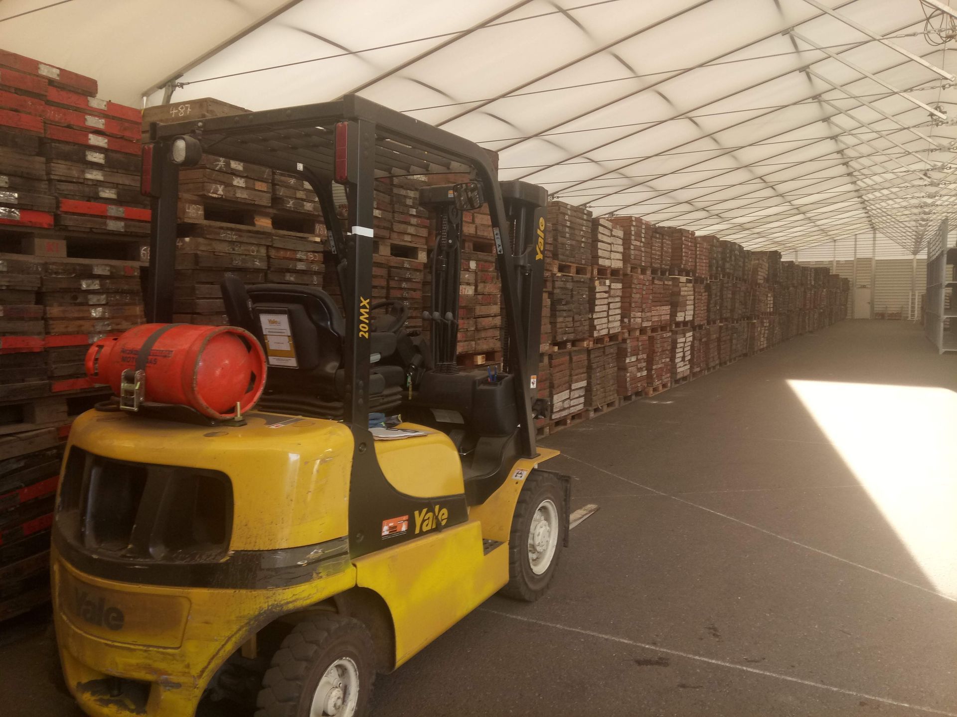 Gelber Gabelstapler in einem Lagerhaus mit gestapelten Paletten voller Ziegelsteine.