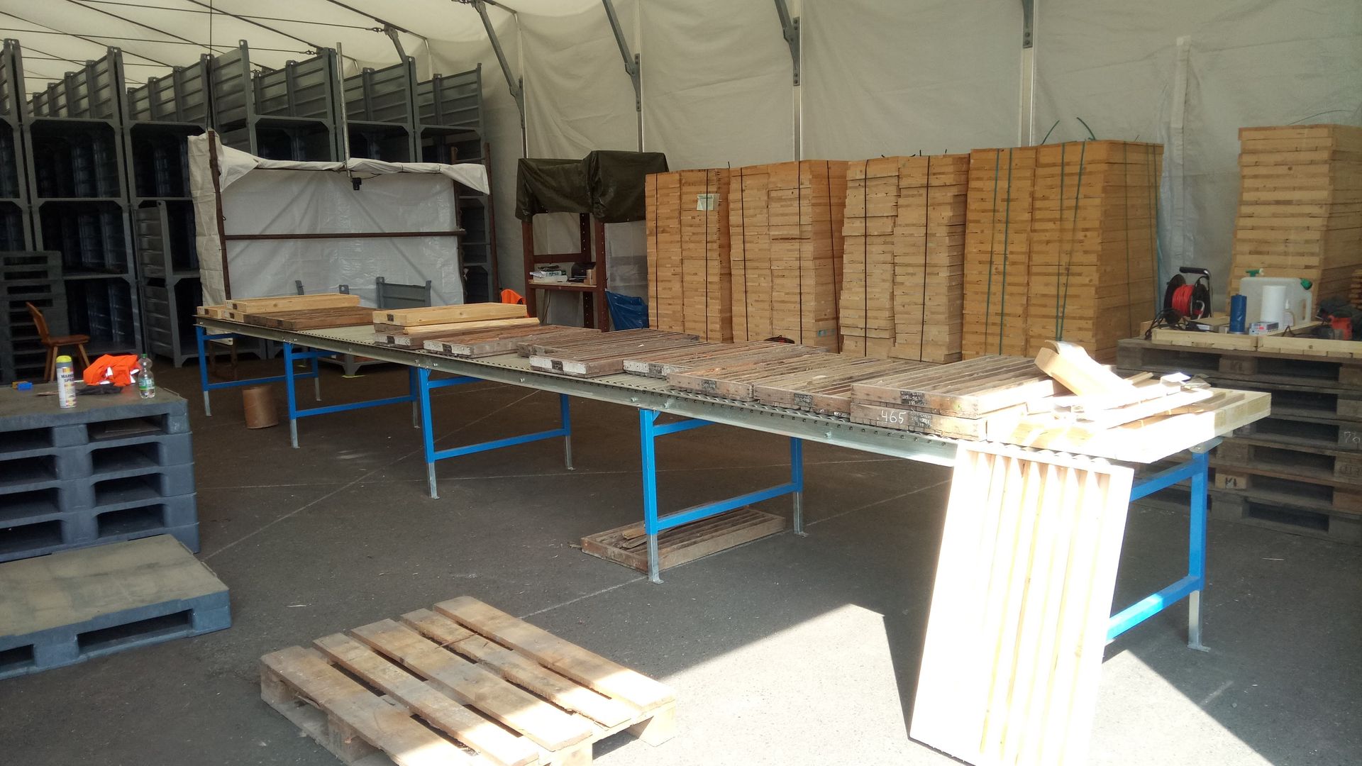 Im Inneren eines großen Zeltes befand sich eine Werkstatt mit Holztischen, Stapeln von Holzkisten und Paletten.