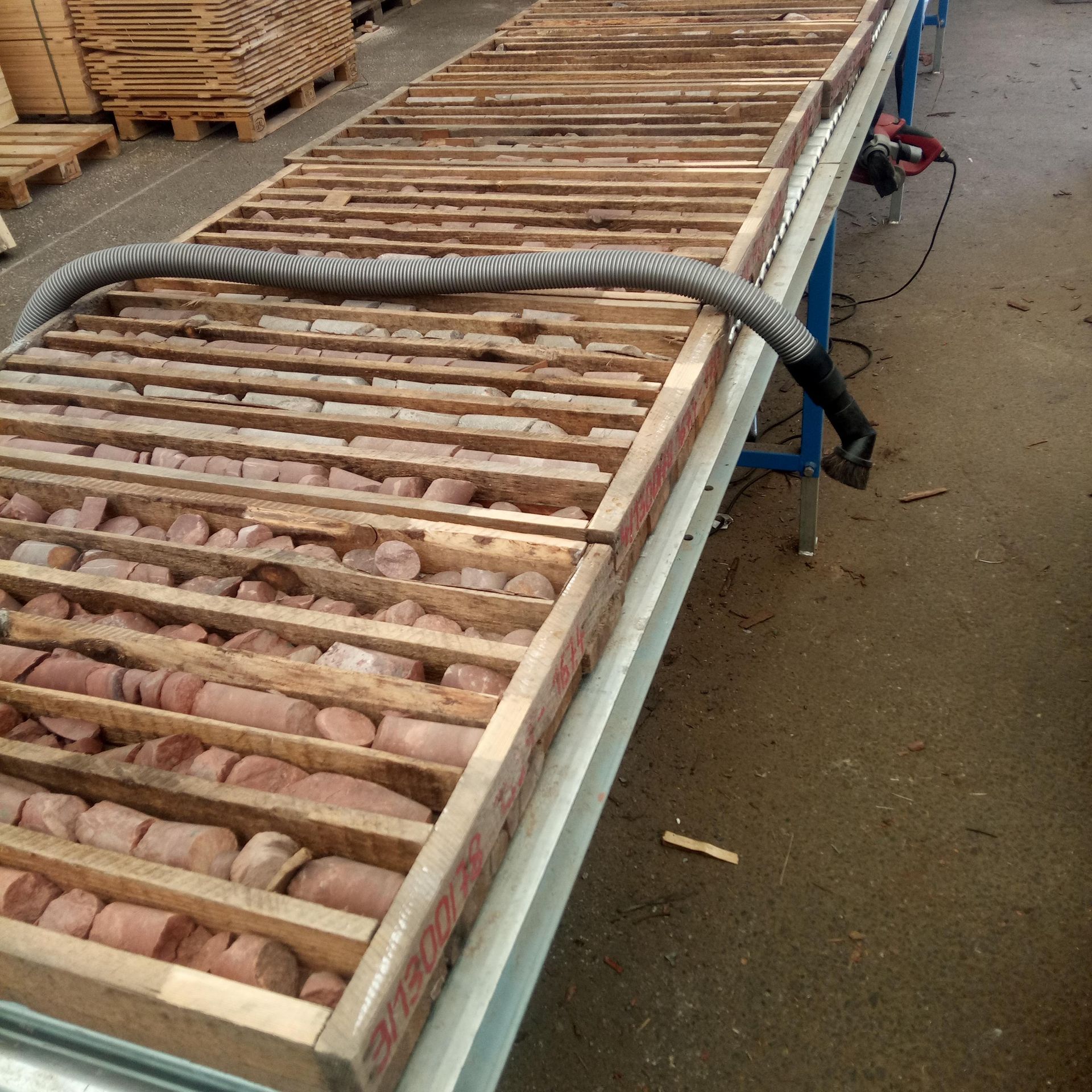 Eine lange Holzkiste enthält mehrere Gesteinskernproben. Die Kiste ist mit Trennwänden und einem Vakuumrohr ausgestattet.