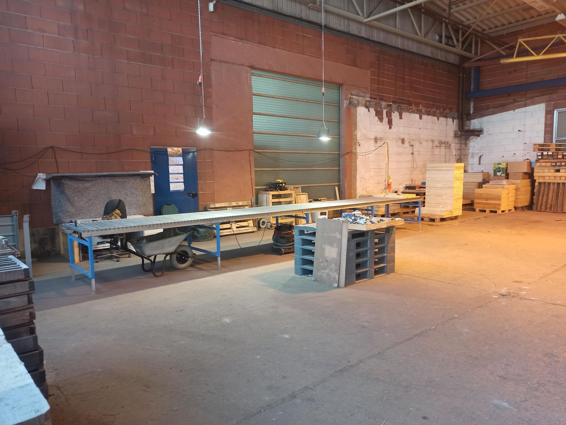 Innenansicht einer Lagerhalle mit Werkbänken, Maschinen, offenem Garagentor, roten Backsteinwänden und Betonboden.
