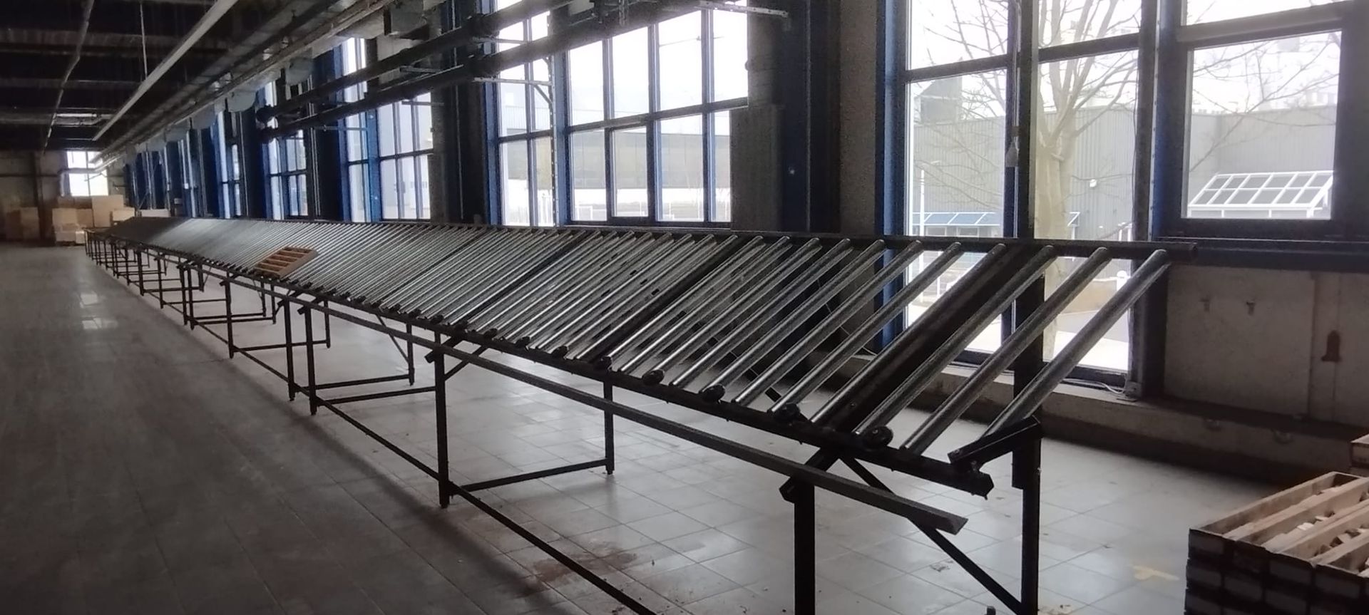 Ein langer Industrietisch mit vielen Metallrohren vor einem Fenster. Ein Raum mit Betonboden.