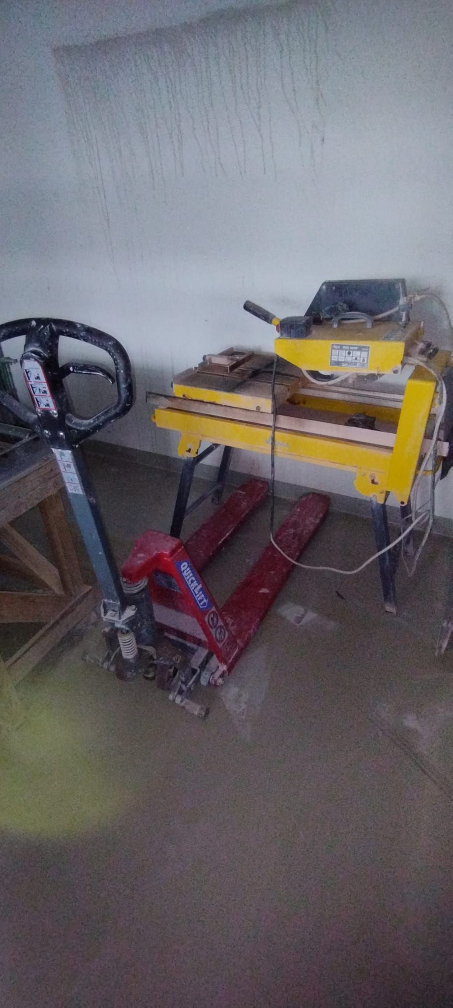 Ein rot-grauer Hubwagen neben einer gelben Fliesensäge in einem Raum.