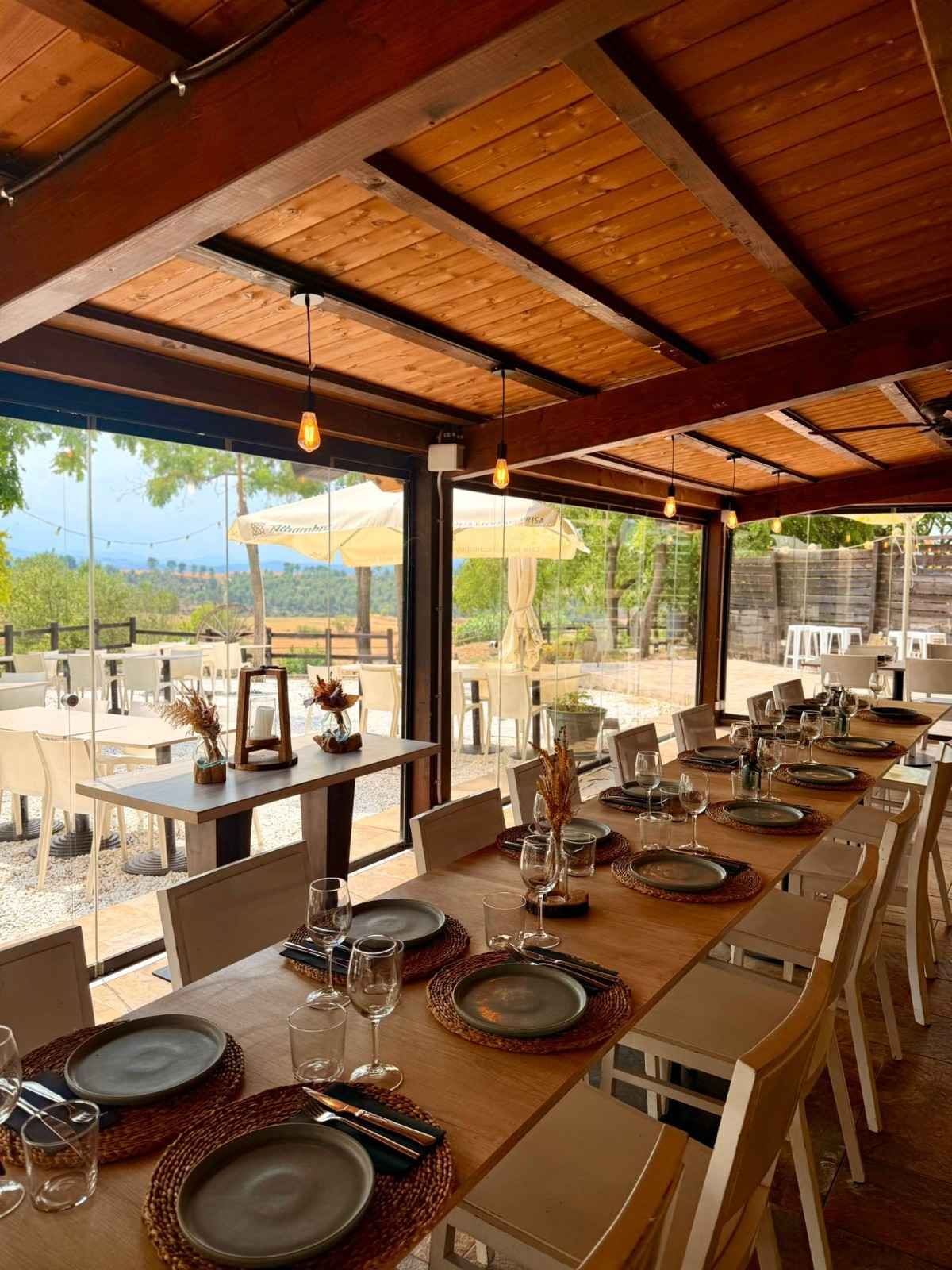 Comedor al aire libre con mesas, vigas de madera y vistas a la montaña.