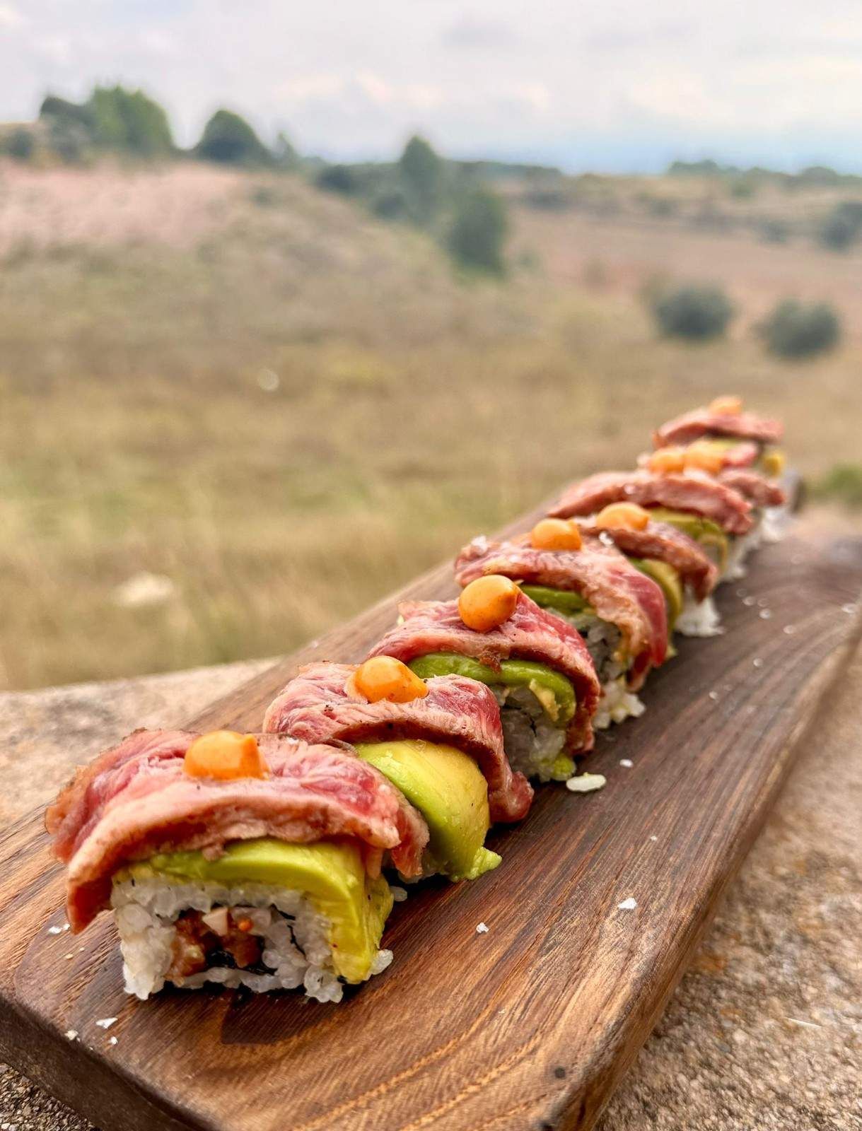 Pastel enrollado en rodajas con cobertura roja y bayas naranjas sobre una tabla de madera al aire libre.