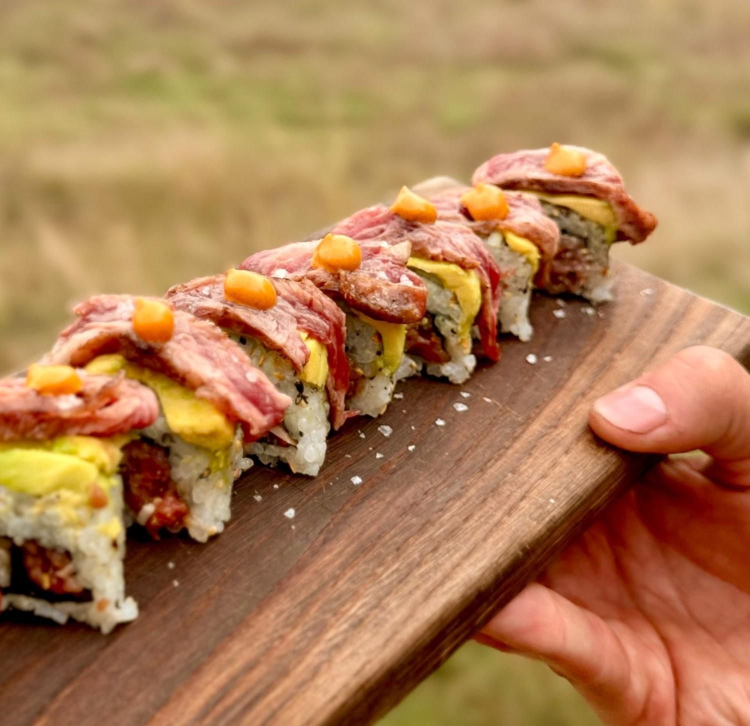 Rollo de sushi cubierto con finas lonchas de salmón y huevas de naranja, servido en una tabla de madera